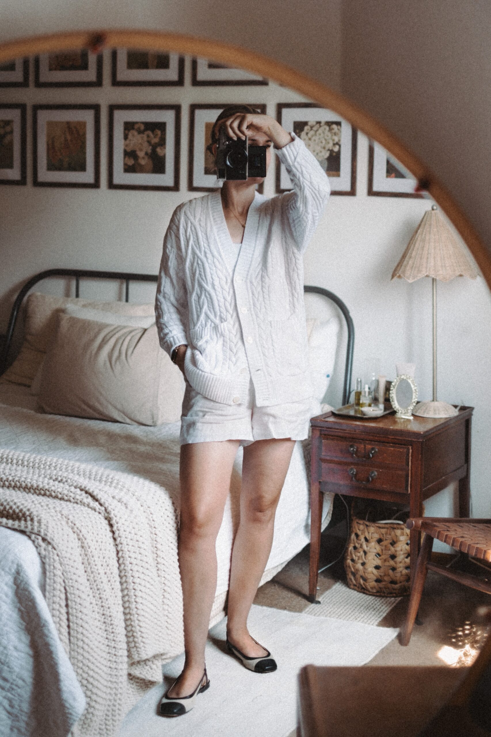 Karin Emily takes a mirror selfie in her room while wear a white cable knit cardigan sweater and white pull on linen shorts from J. Crew