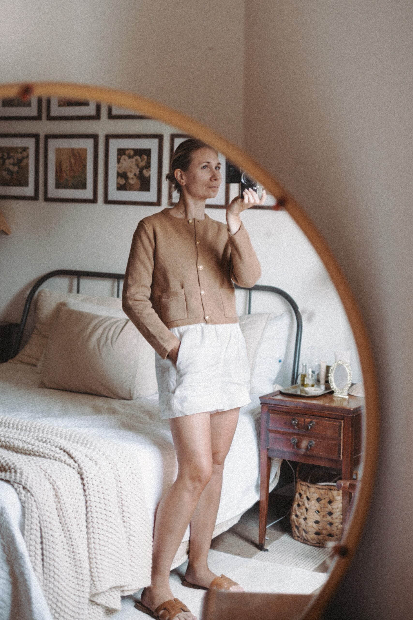 Karin Emily takes a mirror selfie in her room while wearing a camel colored lady cardigan and white pull on linen shorts from J. Crew