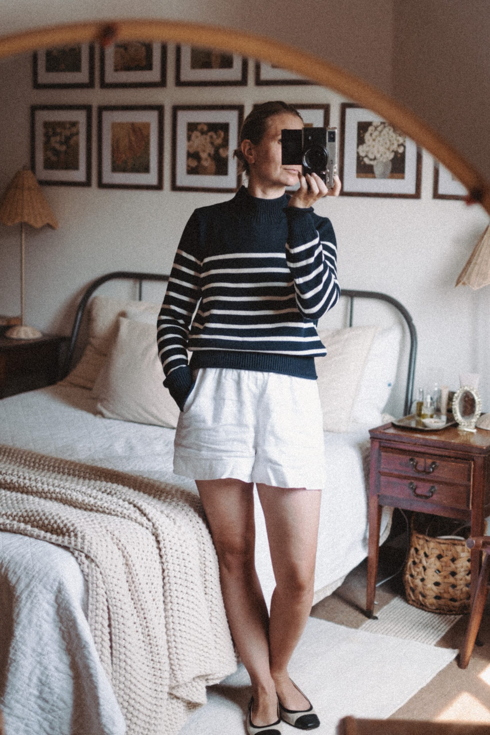 Karin Emily takes a mirror selfie in her room while wearing a navy striped sweater and white pull on linen shorts from J. Crew