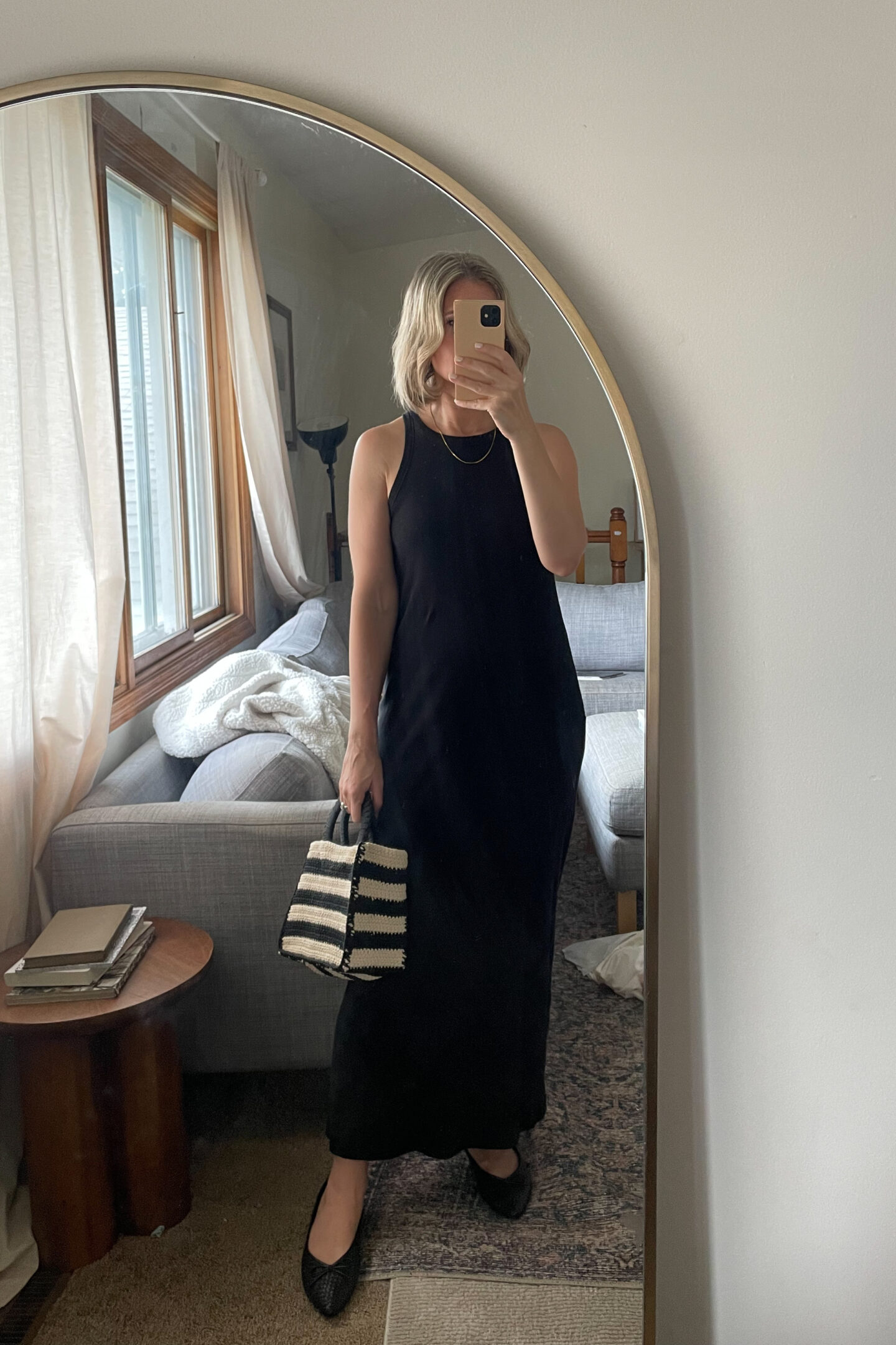 Karin Emily takes a mirror selfie wearing a black tank dress, black woven pointed toe flats and a black and natural colored straw bag