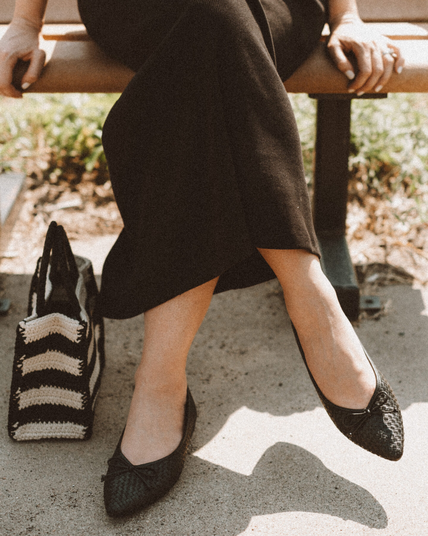 Karin Emily wears a black tank dress and the Birdies Goldfinch flats while standing on a sidewalk in front of a field of wild grasses