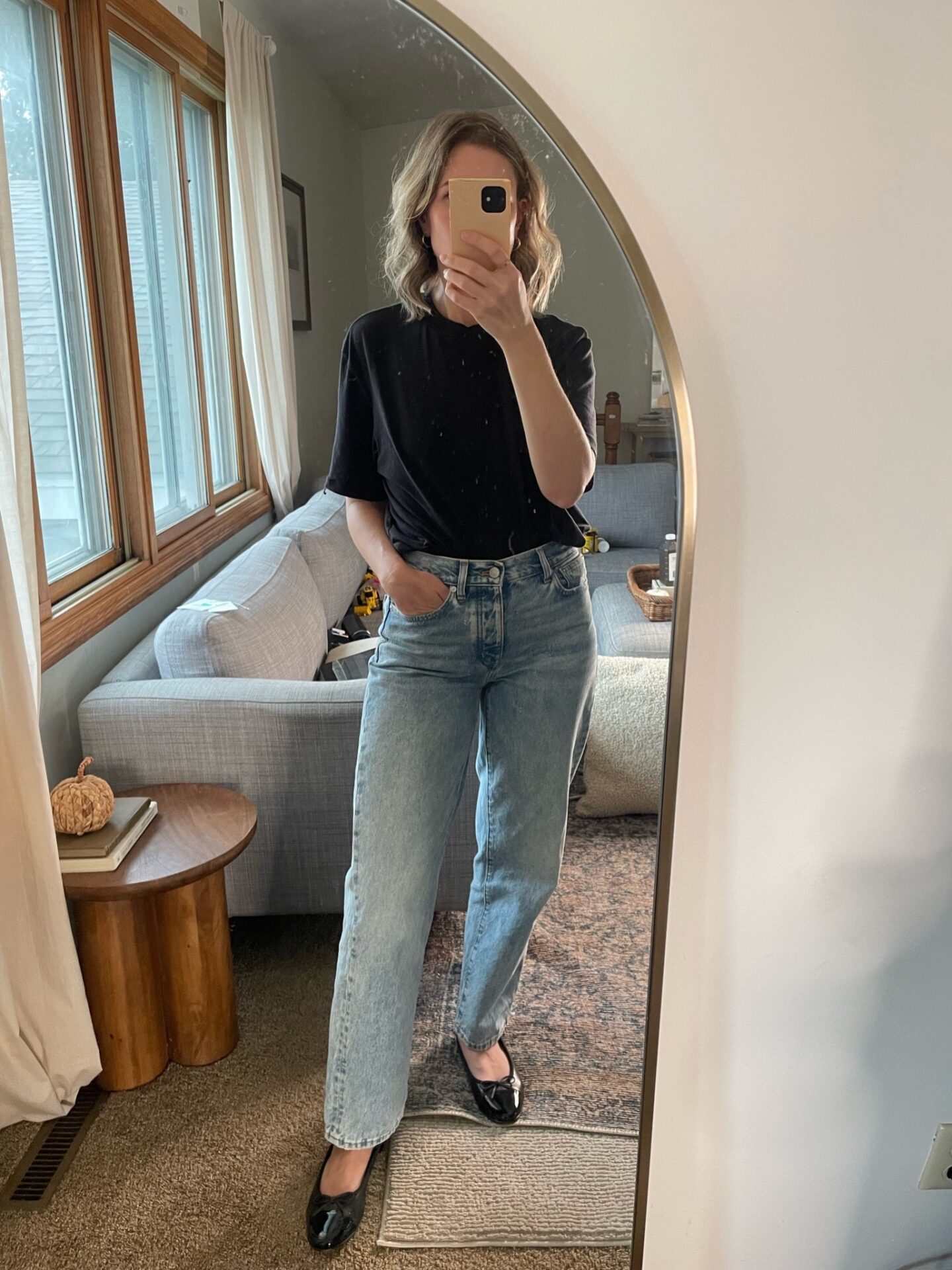 Karin Emily takes a mirror selfie in her living room wearing a black tee with a pair of relaxed jeans and black flats and all three are on sale for Black Friday Sales