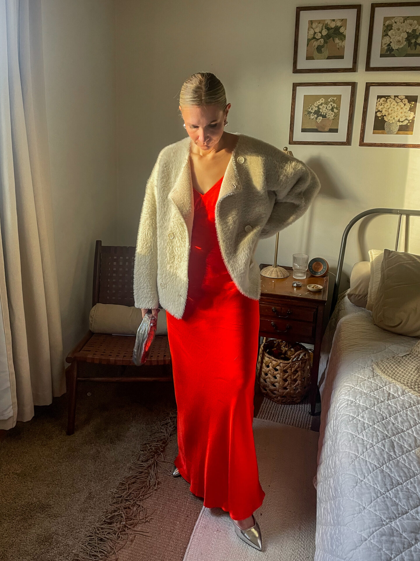 Karin Emily stands in her room wearing a bright red maxi slip dress with a pair of silver shoes and a faux fur drape coat