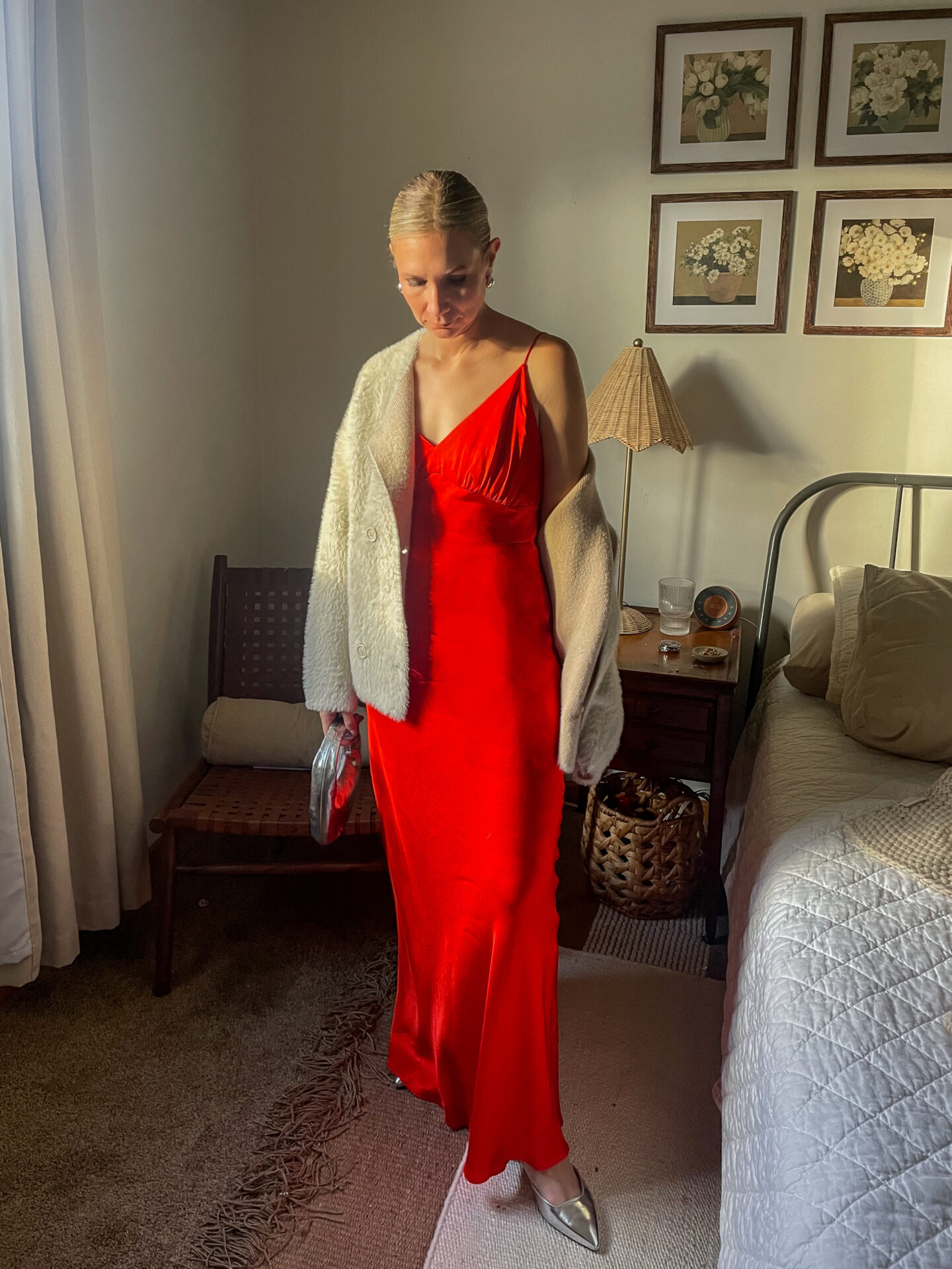 Karin Emily stands in her room wearing a bright red maxi slip dress with a pair of silver shoes and a faux fur drape coat