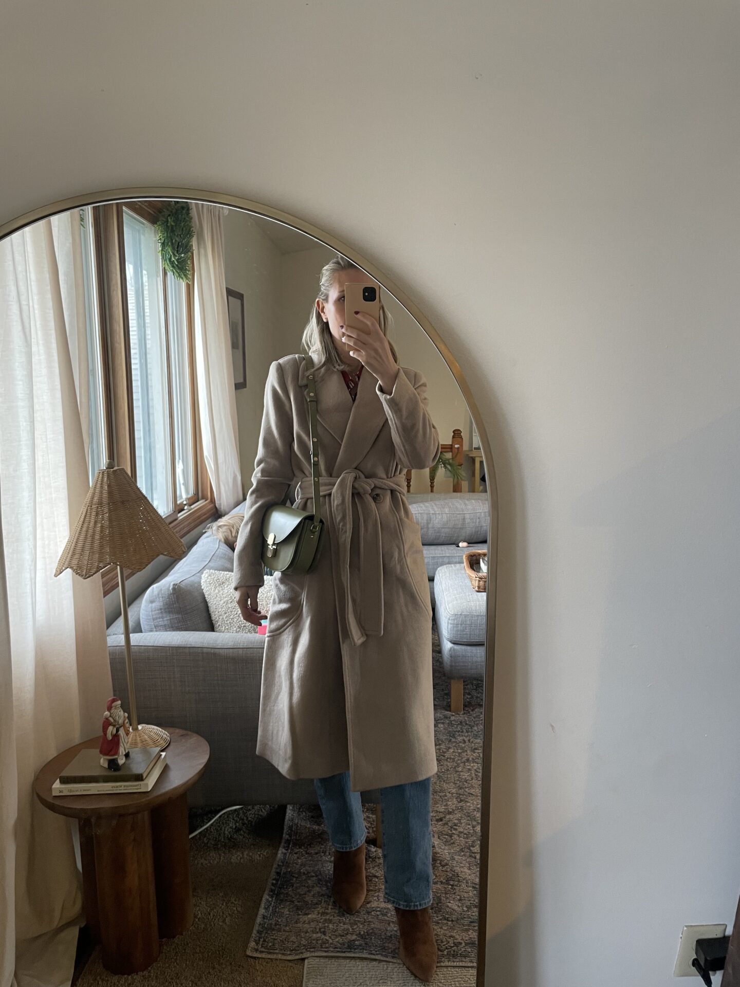 Karin Emily wears a tan wool coat over a burgundy button down with straight leg jeans with brown boots