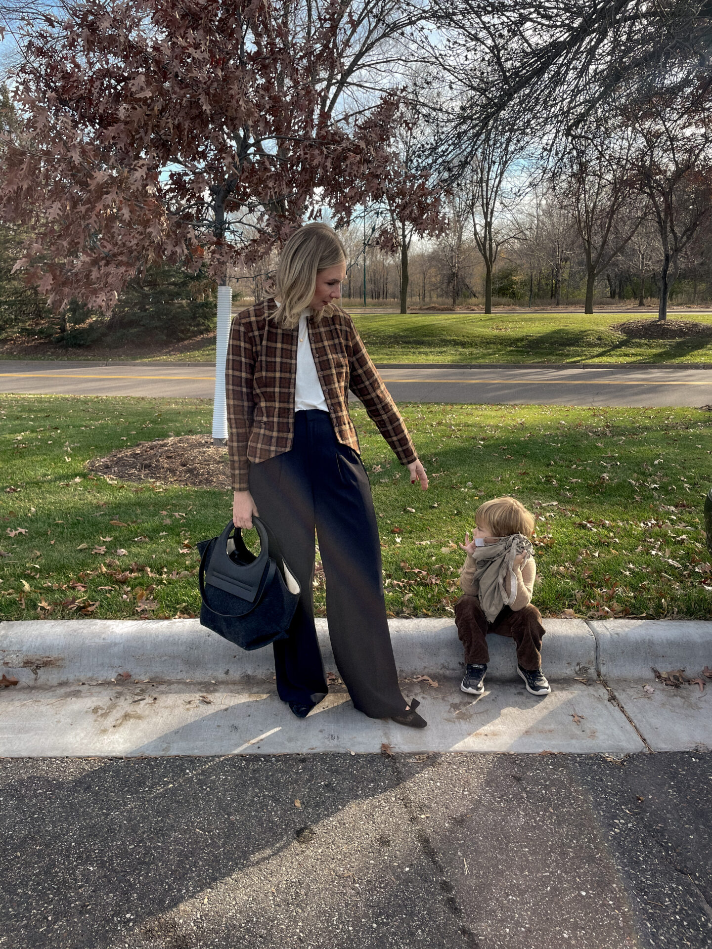 Karin Emily stands on a curb with her son and wears a plaid blazer and white tee with black wide leg pants and black bow flats and all are on sale for Black Friday Sales