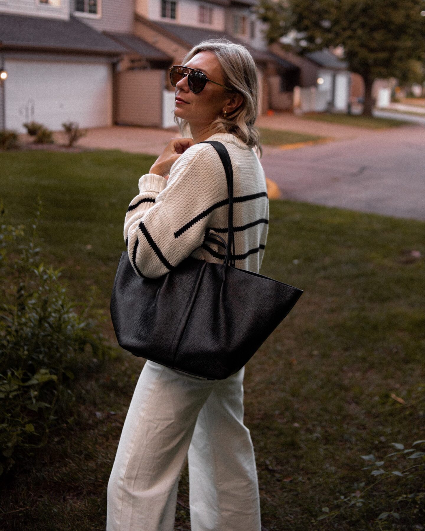 Karin Emily wears a striped sweater with cream wide leg pants and a black handbag