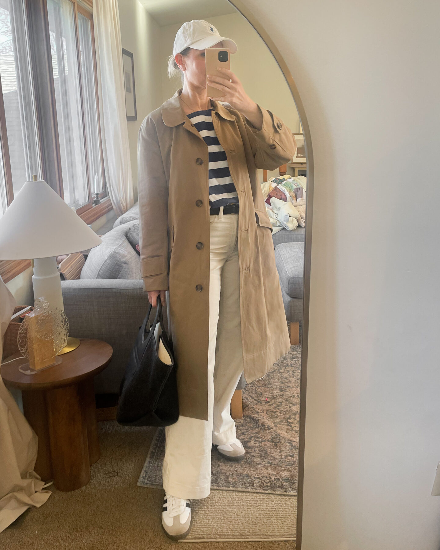 Karin Emily wears a trench coat with cream jeans and sneakers and a striped tee from Sezane 