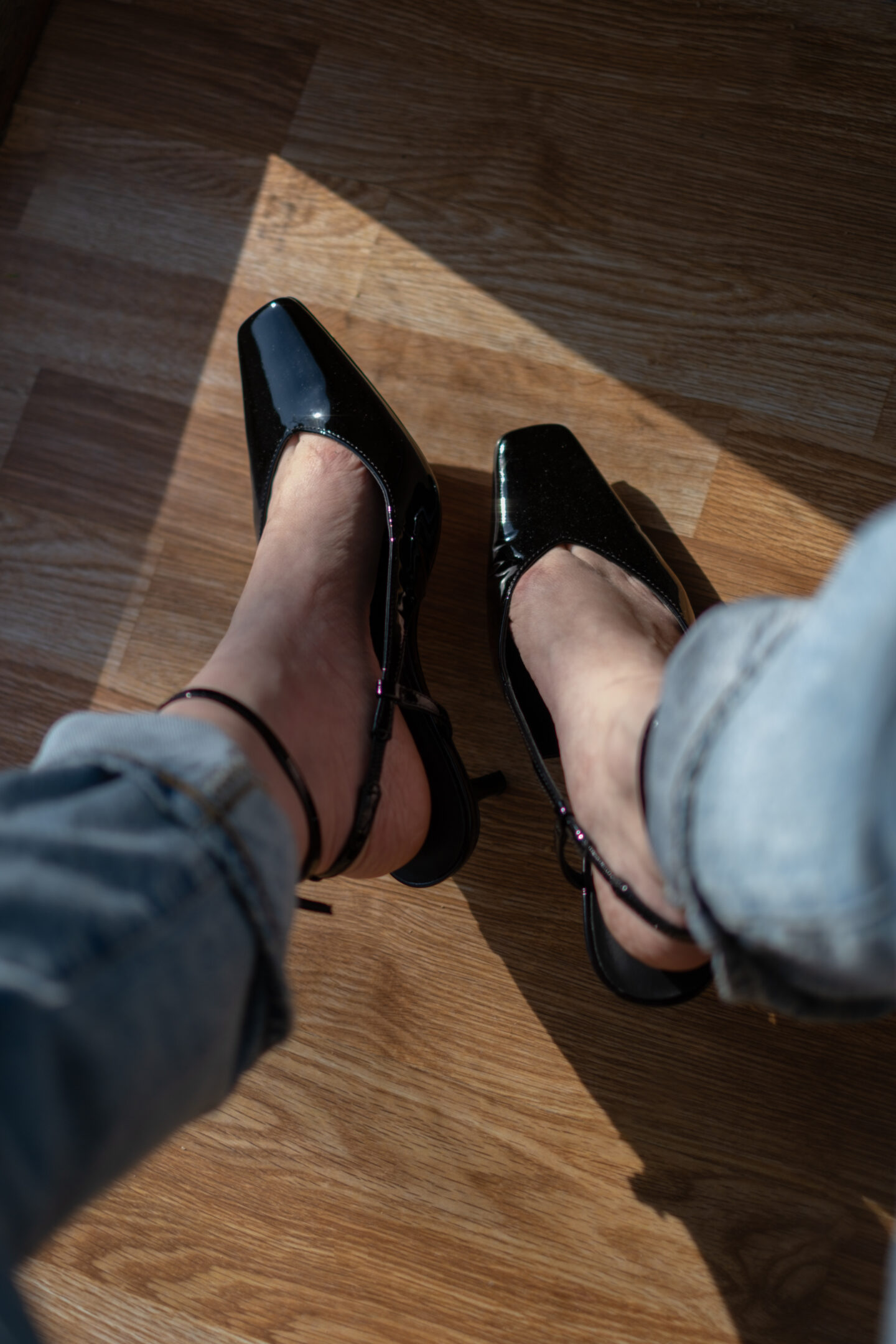 A pair of black patent leather sling back heels with a pair of cuffed jeans