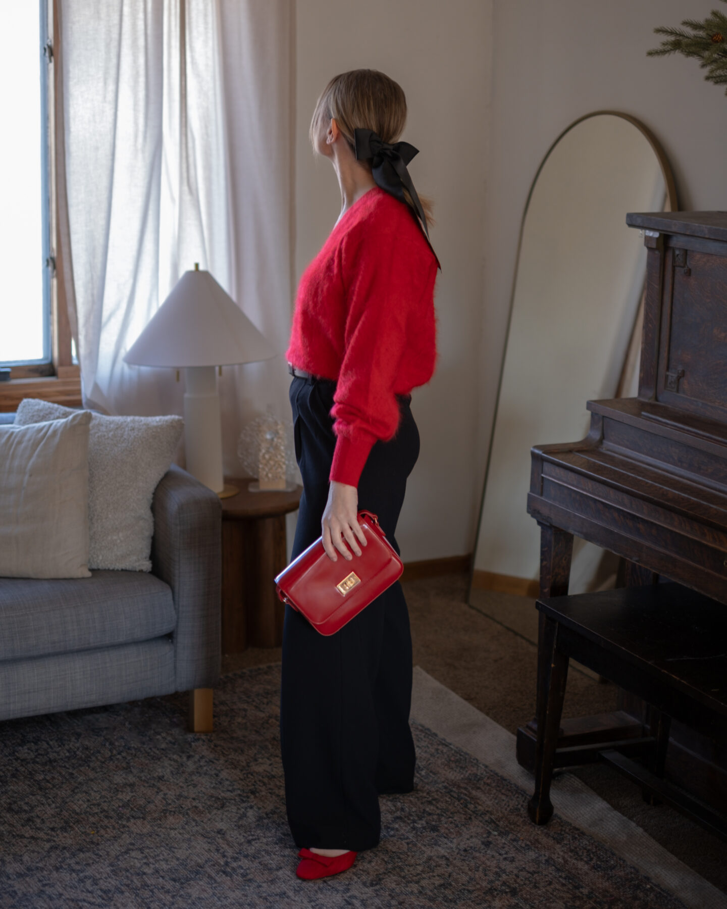 Karin Emily wears a soft red cashmere sweater with wide leg black pants and modern black heels with a bow in her hair for a date night 