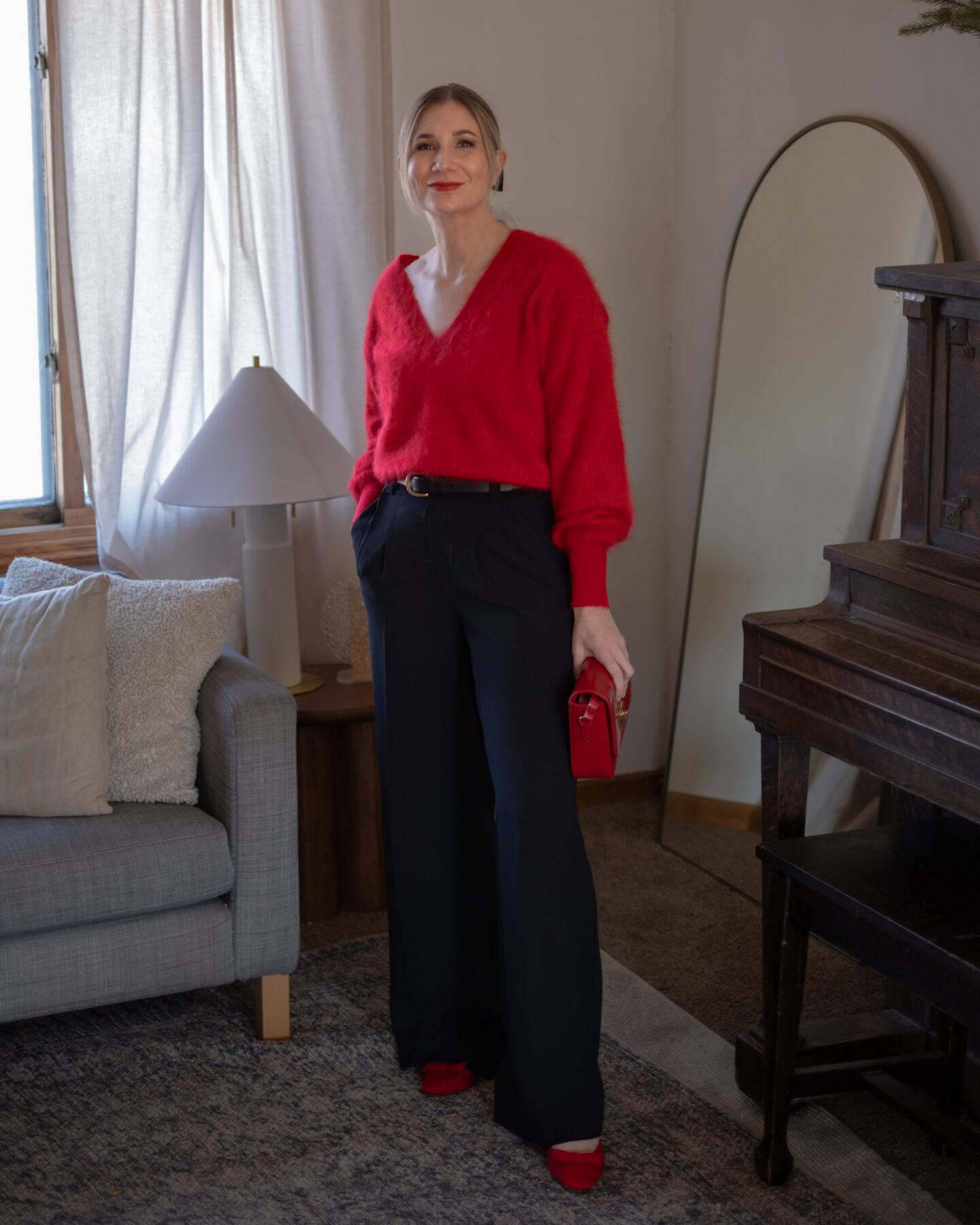 Karin Emily wears a soft red cashmere sweater with wide leg black pants and modern black heels with a bow in her hair for a date night 