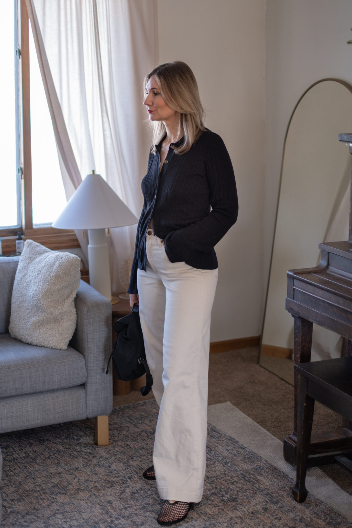 Karin Emily wears her white jeans for spring with a black ribbed cardigan and mesh flats