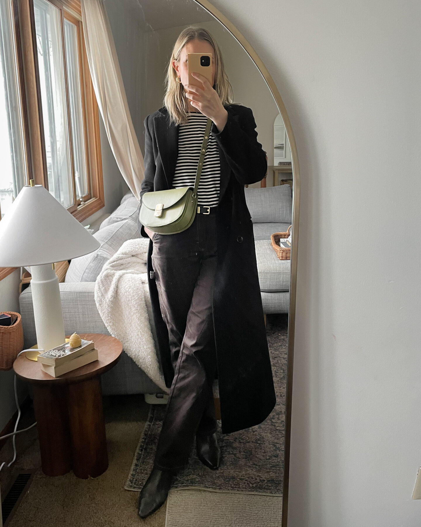 Karin Emily takes Amira selfie for some recent outfits, wearing a striped tea with a long black wool coat over a pair of brown cargo pants, brown pointed toe booties, and a green Sezane bag