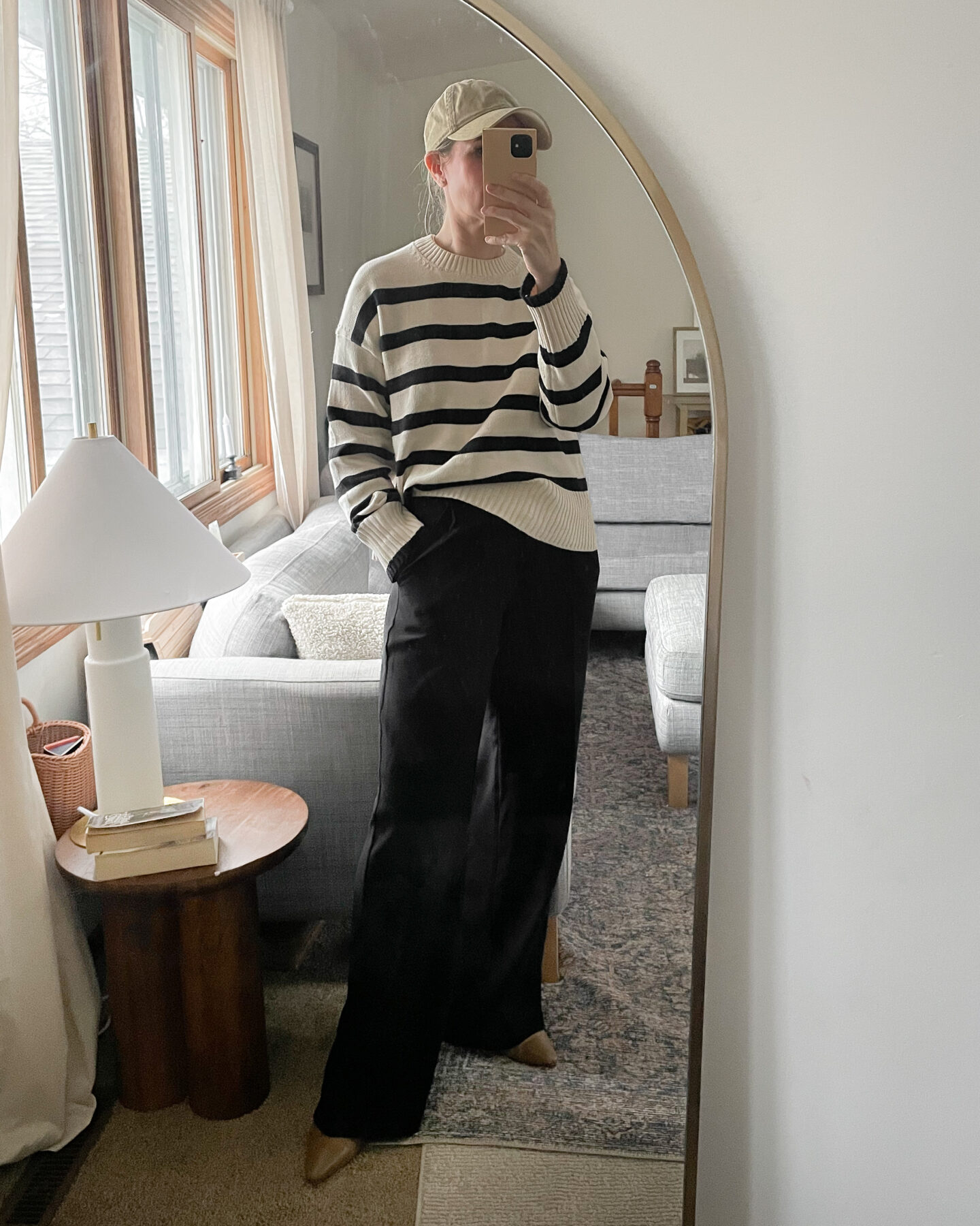 Karin Emily personal style wears a striped sweater from Everlane over a pair of black pleated pants with a pair of brown pointed toed booties and a tan colored baseball hat for a recent post about recent outfits