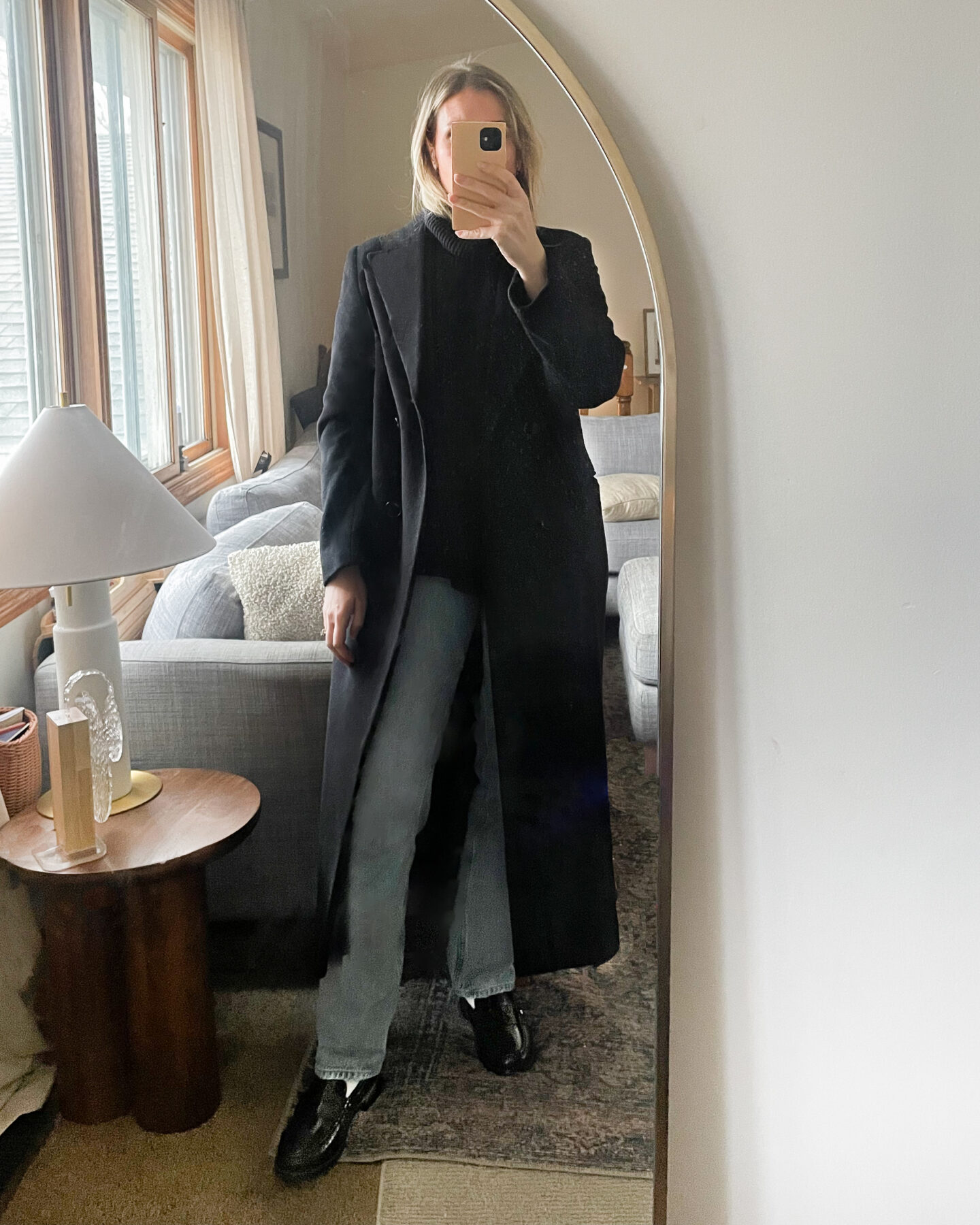 Karin Emily wears a long black wool maxi coat over a black turtleneck sweater. A pair of light wash Lana jeans from agolde and a pair of black loafers from Freda Salvador.