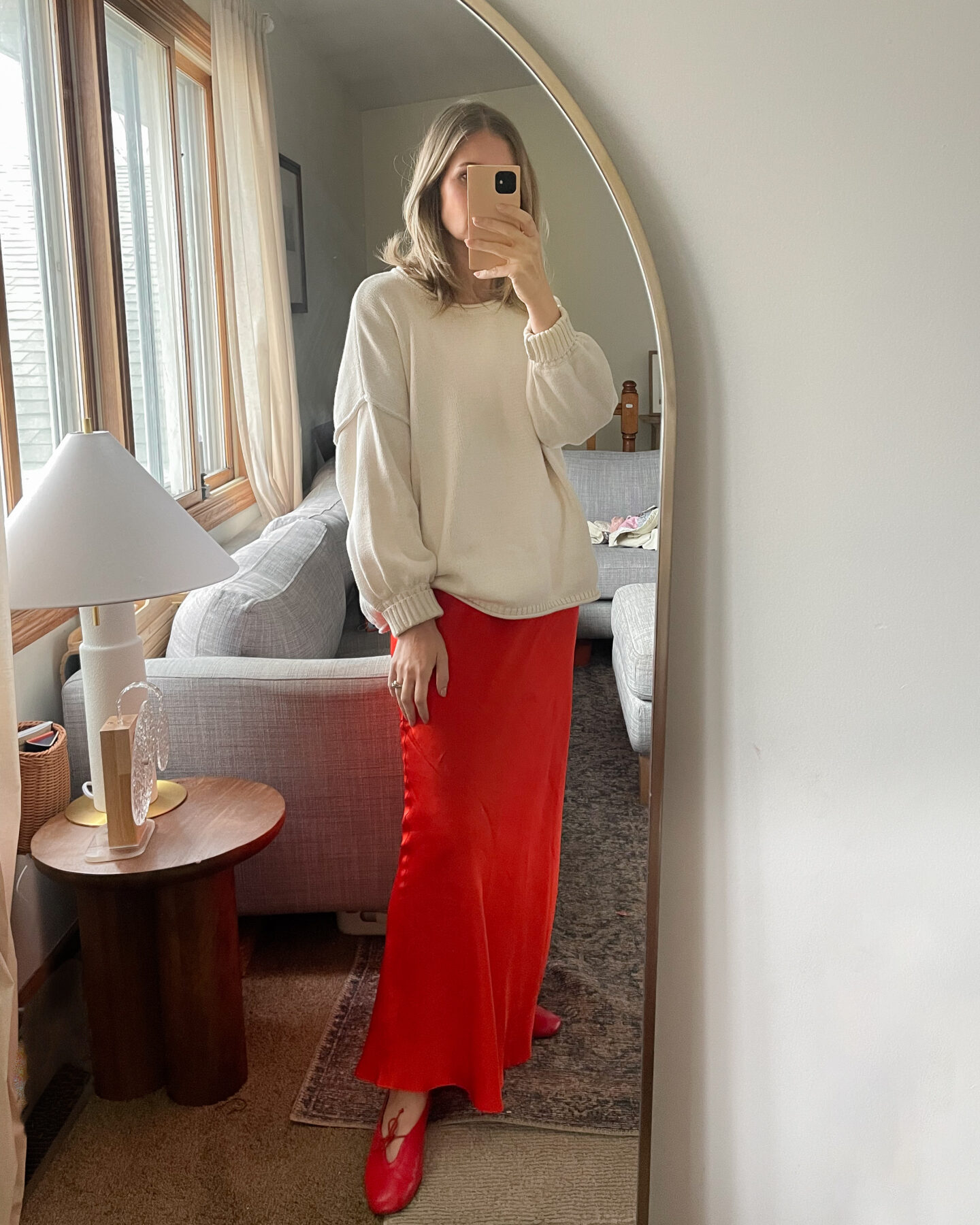 Karen Emily wears an oversized cream sweater over a red slip dress with a pair of red flats with bows on them for a recent post about recent outfits