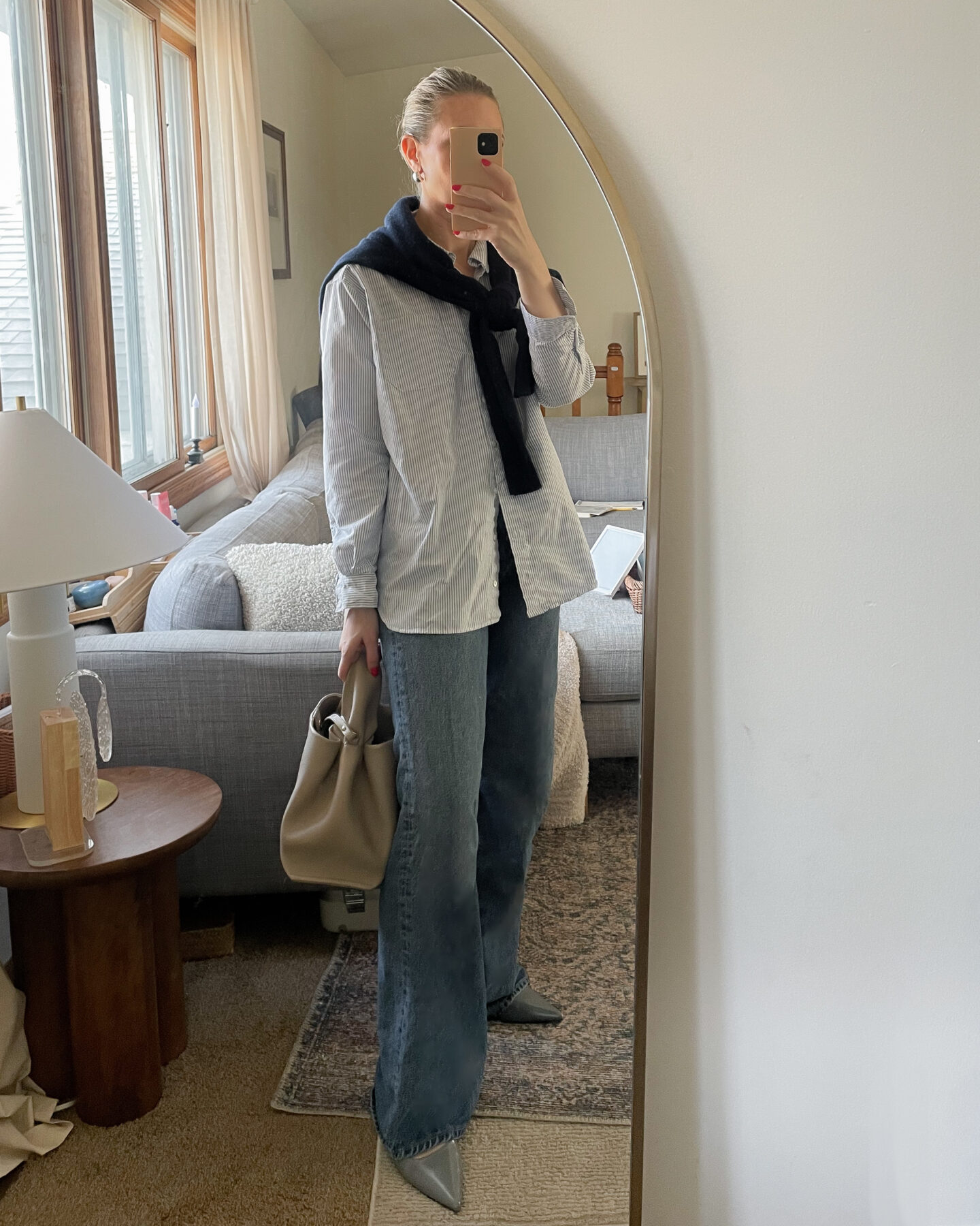 Karin Emily personal style wears an oversized blue and white striped button-down shirt from Sezane over a pair of baggy wide leg pants with a pair of gray pointed toe flats and a navy blue cashmere sweater worn as a scarf with a gray polene bag for a recent post about recent outfits