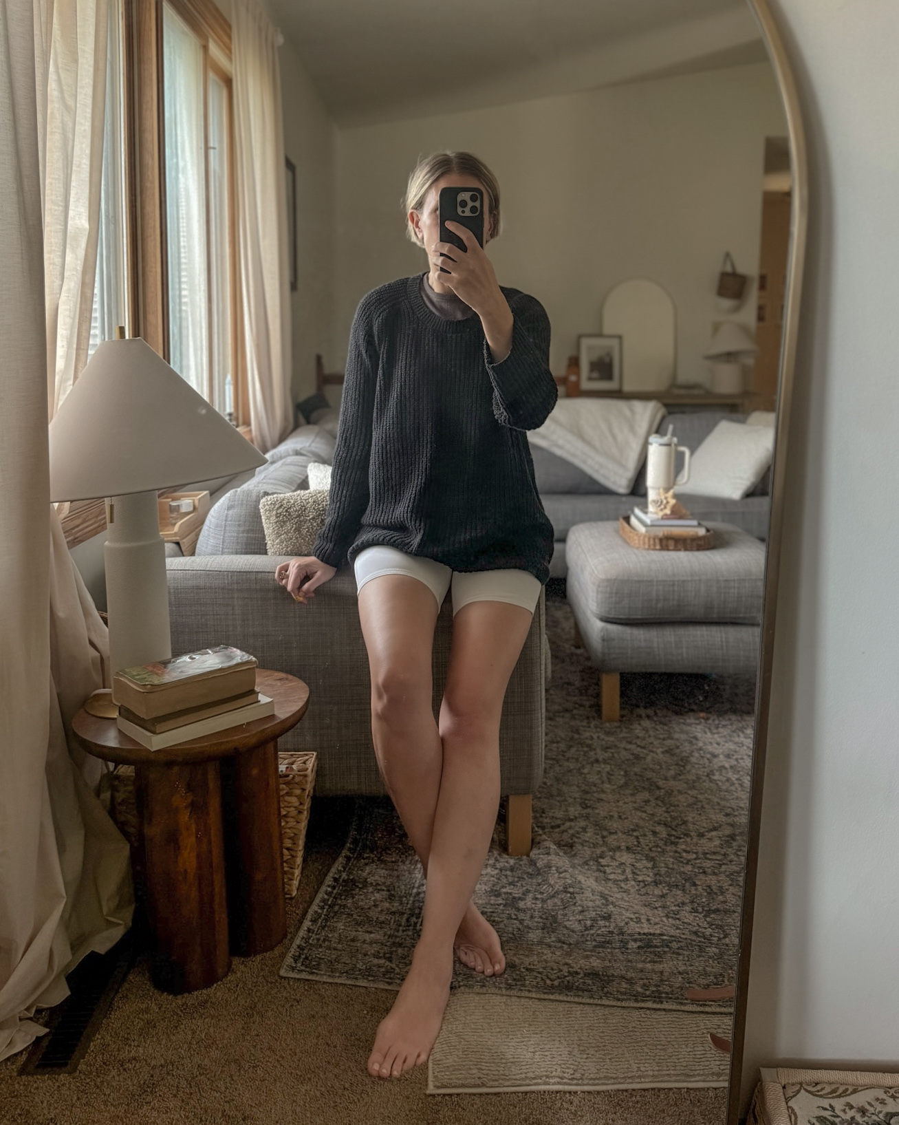 Karin Emily shares a mirror selfie of herself wearing an oversized black cotton sweater over a pair of white bike shorts 