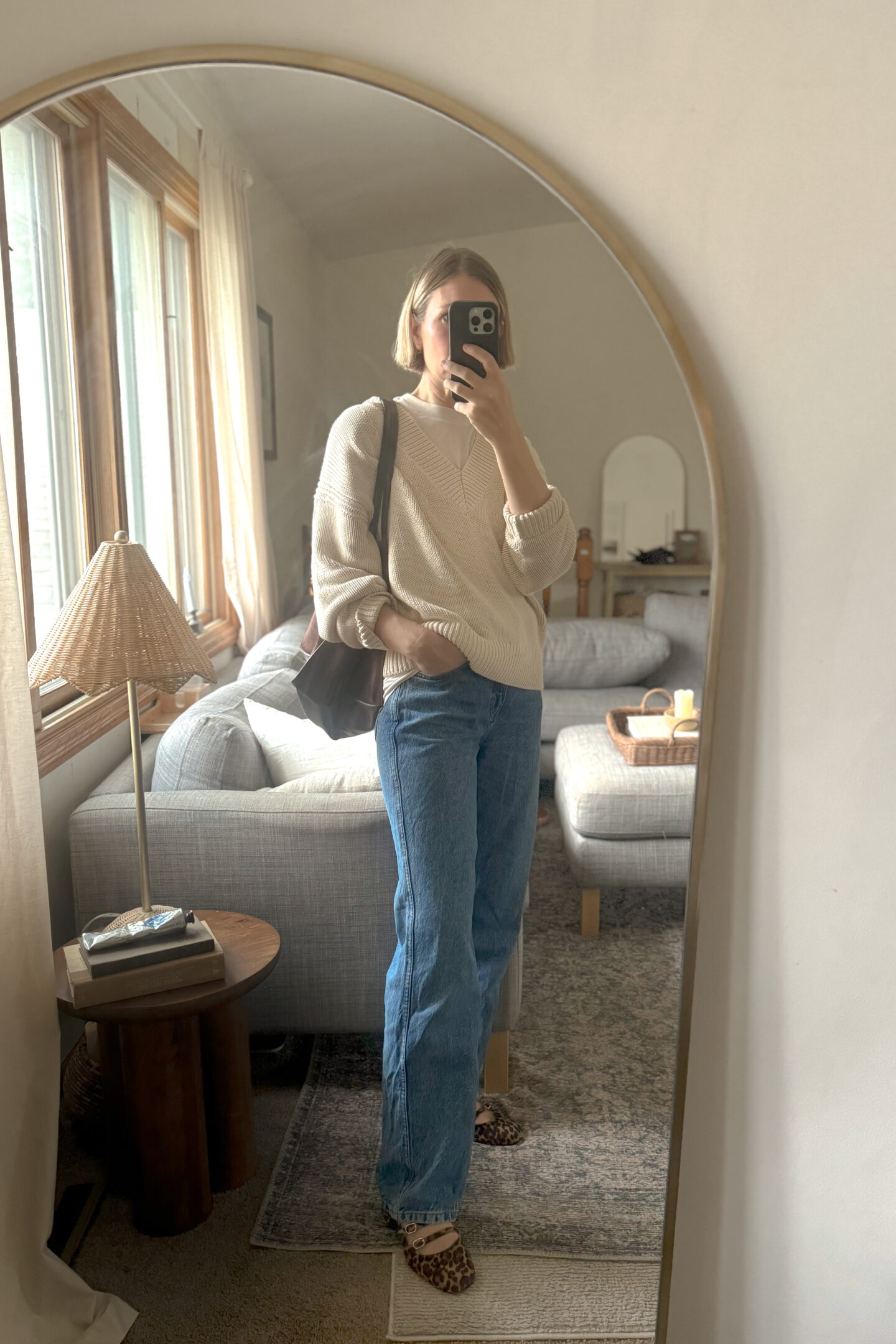 Karin Emily is selling all of her clothes but is still left with a cream oversized cotton sweater, a pair of dark wash baggy jeans, a pair of leopard print heels from Sezane, and a chocolate brown suede tote bag