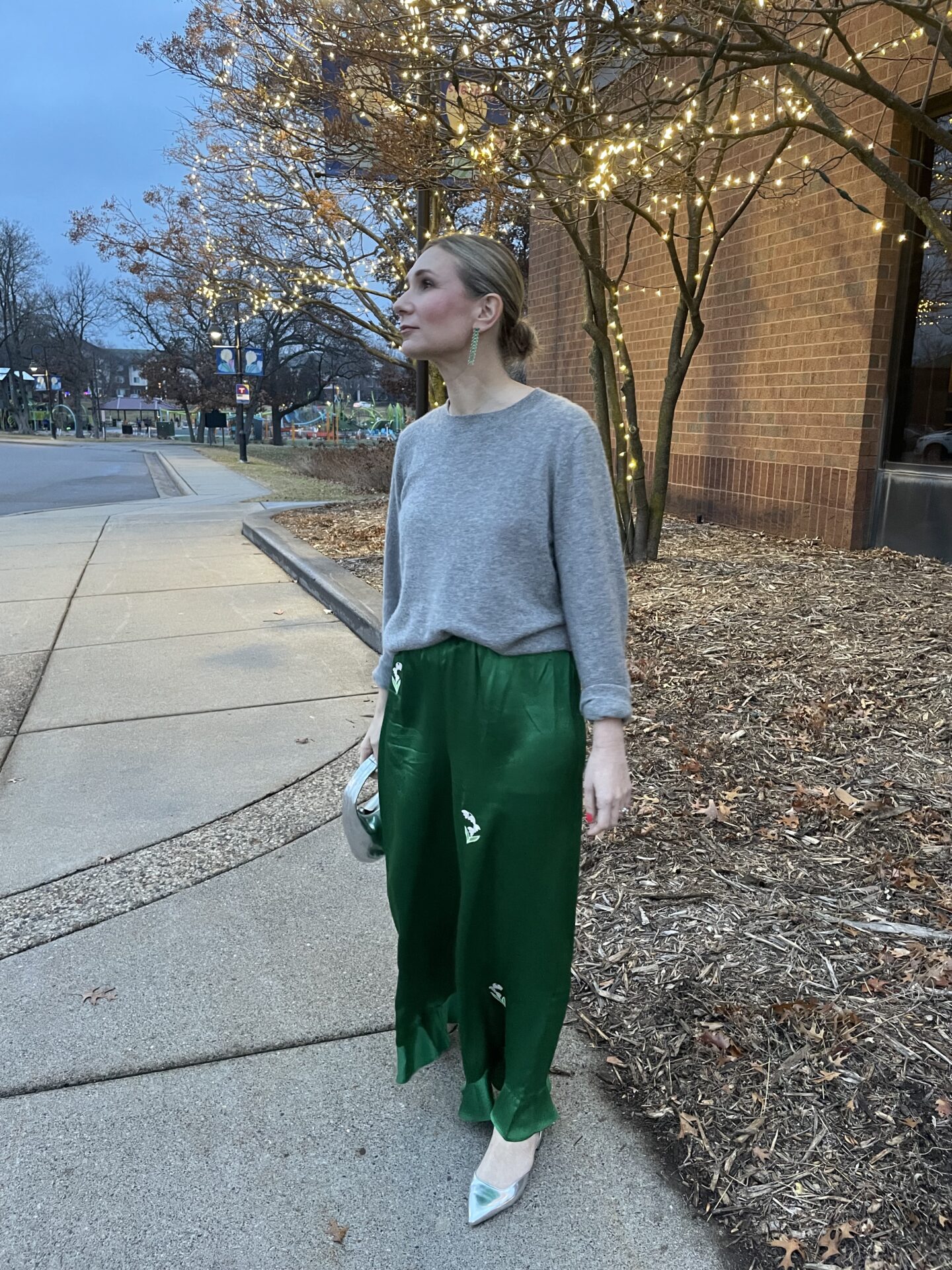 Karin Emily wears a festive holiday outfit with a pair of Doen green silk pants, a cashmere sweater, and silver accessories