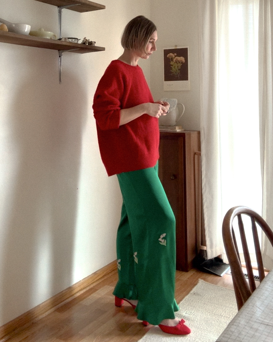 Karin Emily shares her 2024 sparkly edit while standing in her kitchen wearing a Christmas red cashmere sweater, a pair of silk green pants and red bow heels