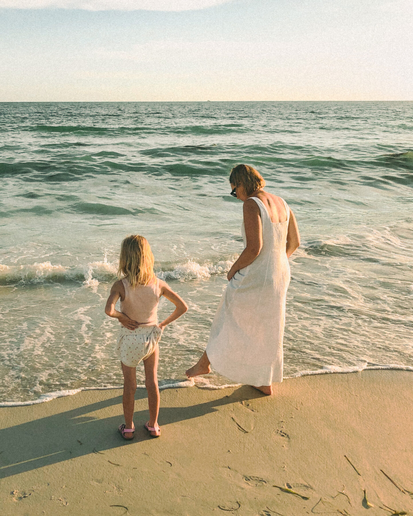 Karin Emily stands at the ocean with her young daughter right as a wave laps their feet. in this blog post she talks about having a hysterectomy and what life is like with four neurodivergent children.